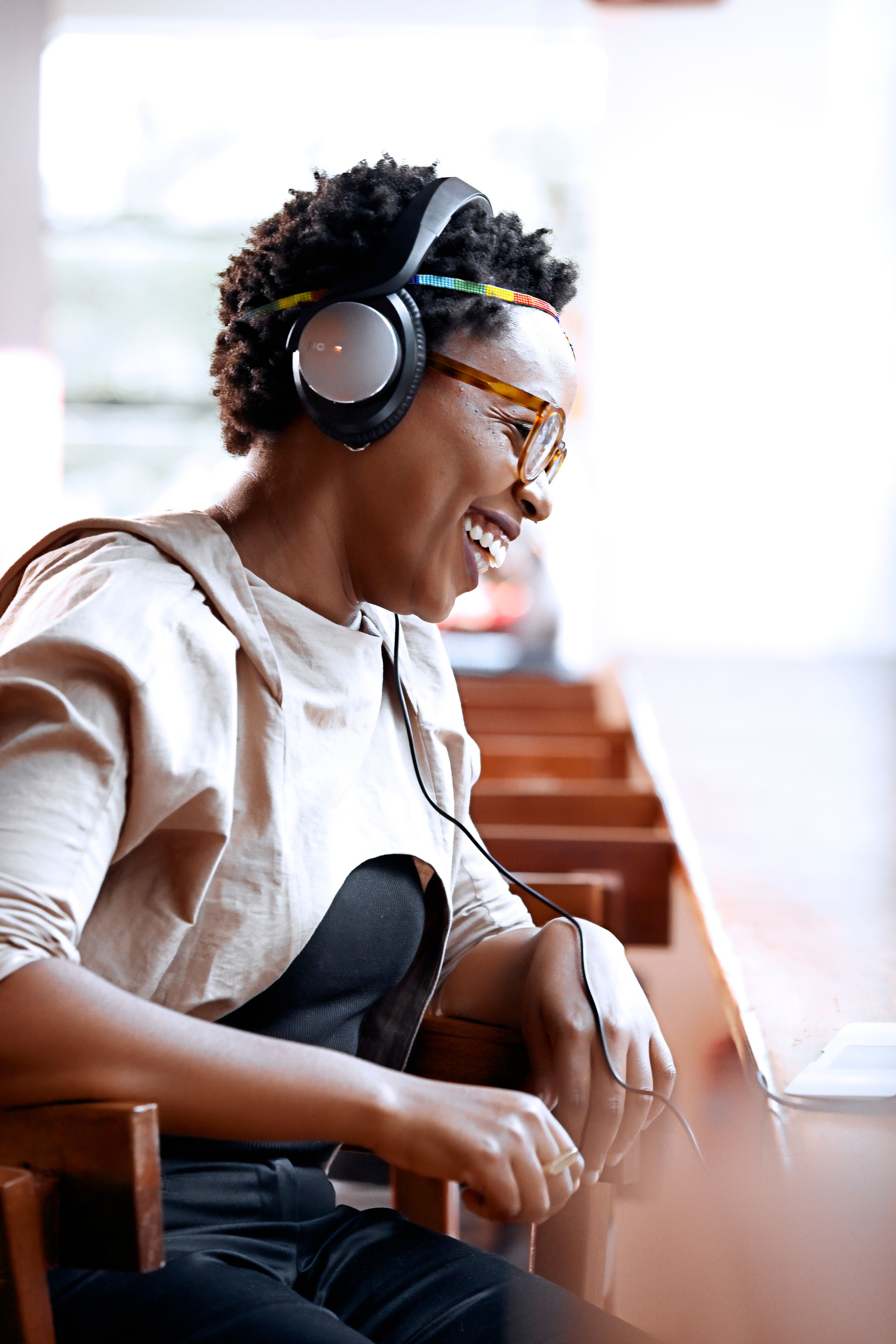 A woman wearing headphones sits by a sunlit window.